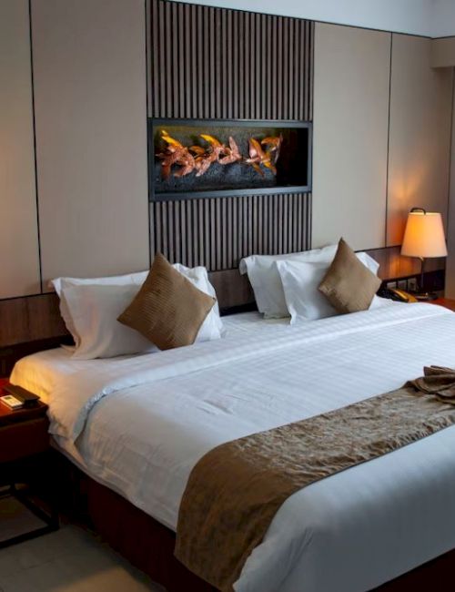 A cozy hotel room with a large, neatly made bed, decorative pillows, bedside lamps, a small table, and a window with curtains.