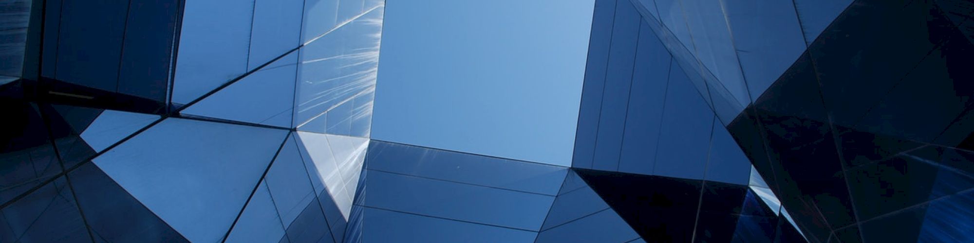 The image shows a pattern of skyscrapers forming a geometric space with a small portion of the sky visible in the center of the view.