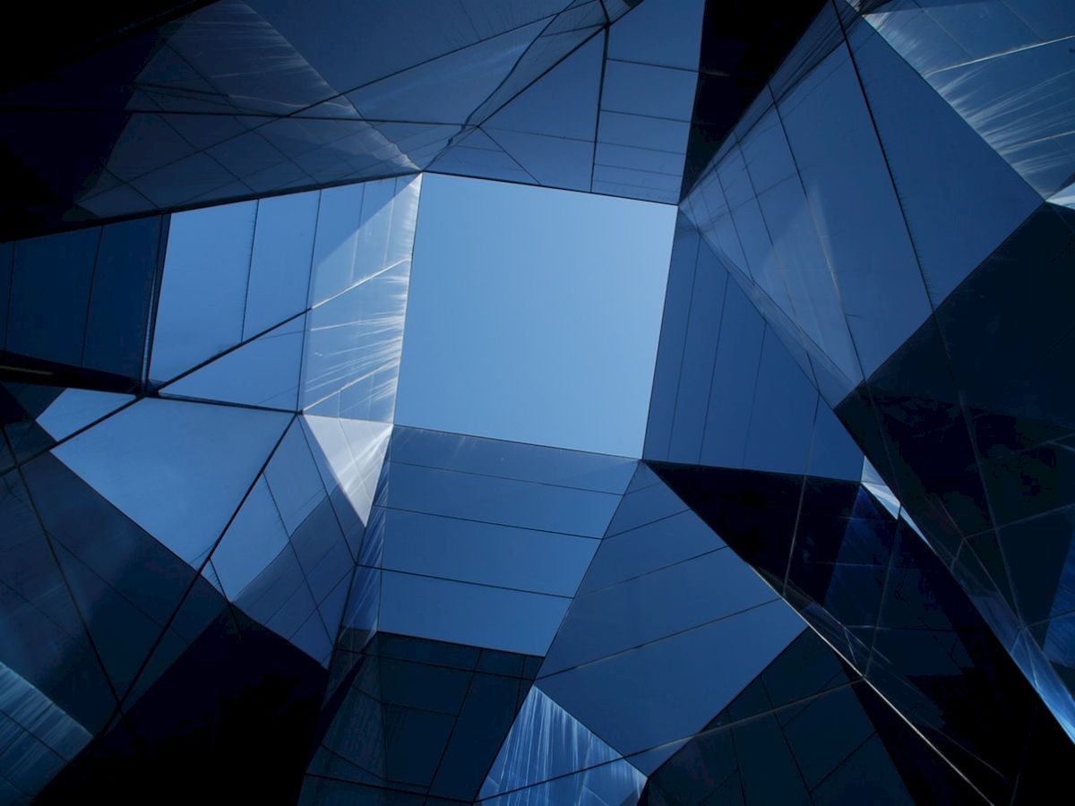 The image shows a geometric pattern created by several reflective glass surfaces forming an open hexagon against a backdrop of blue sky.