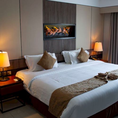 A neatly arranged hotel room with a large bed, two bedside tables with lamps, a wall-mounted decorative piece above the bed, and curtains by the window.