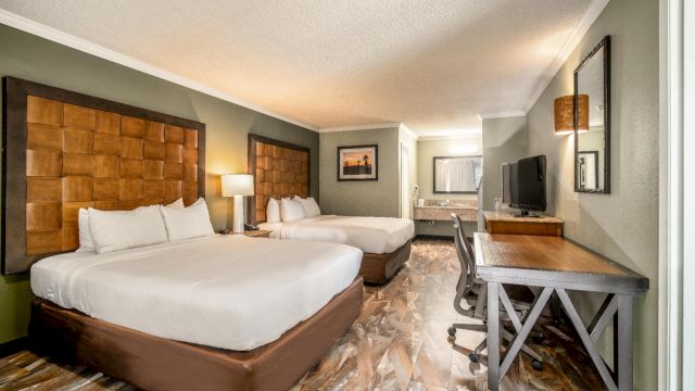 A hotel room with two beds, a desk, and a TV.