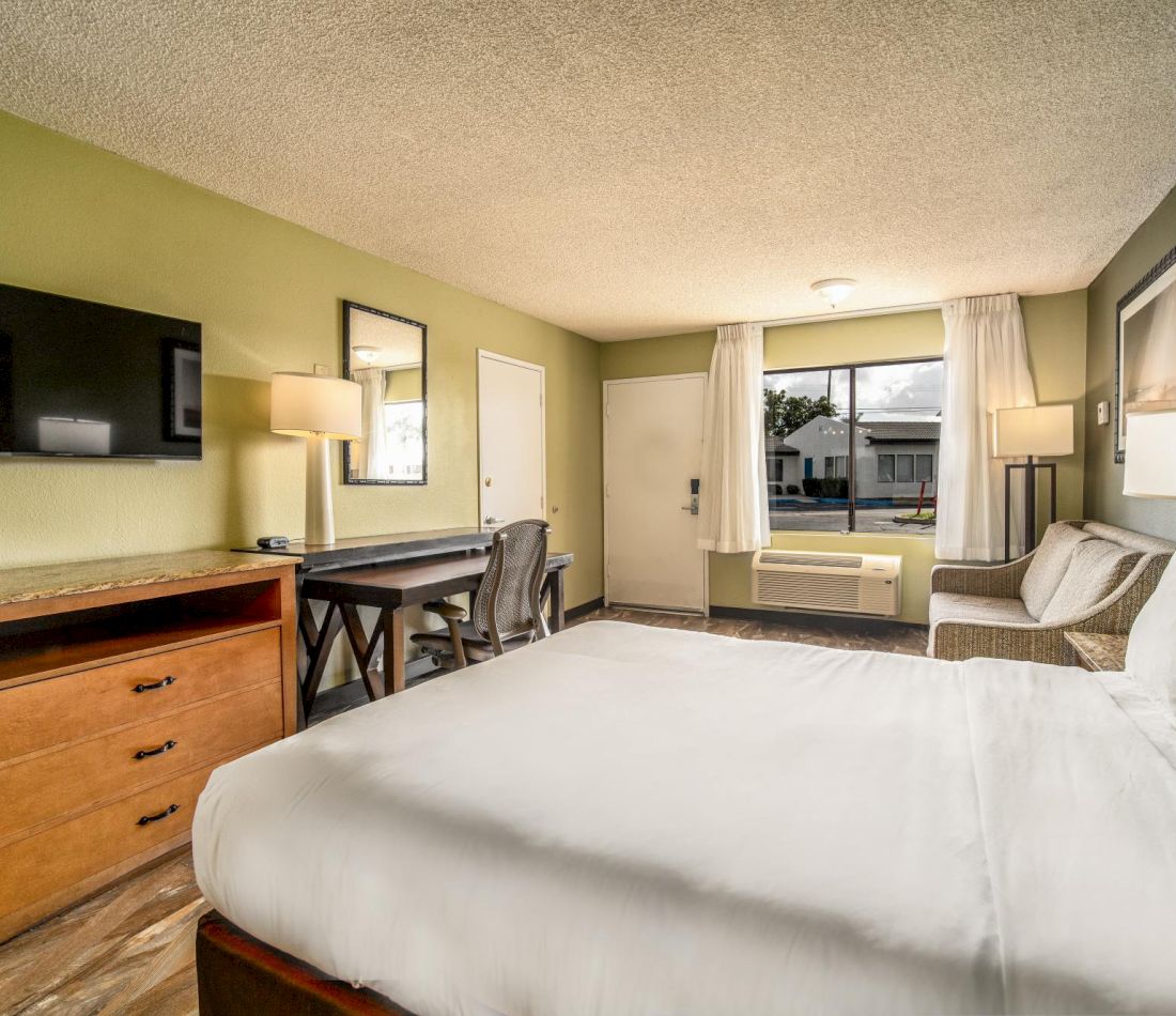 A hotel room with a bed, desk, TV, and window