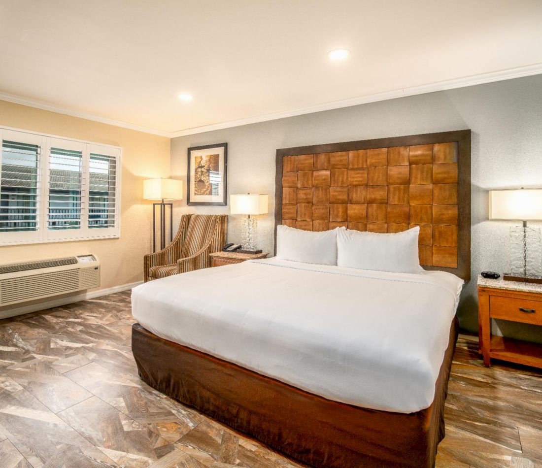 A hotel room with a large bed, two nightstands, a chair, and a window.