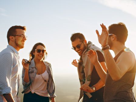 Four people are outside, smiling and laughing. They seem to be having a joyful time together, enjoying each other's company in daylight.