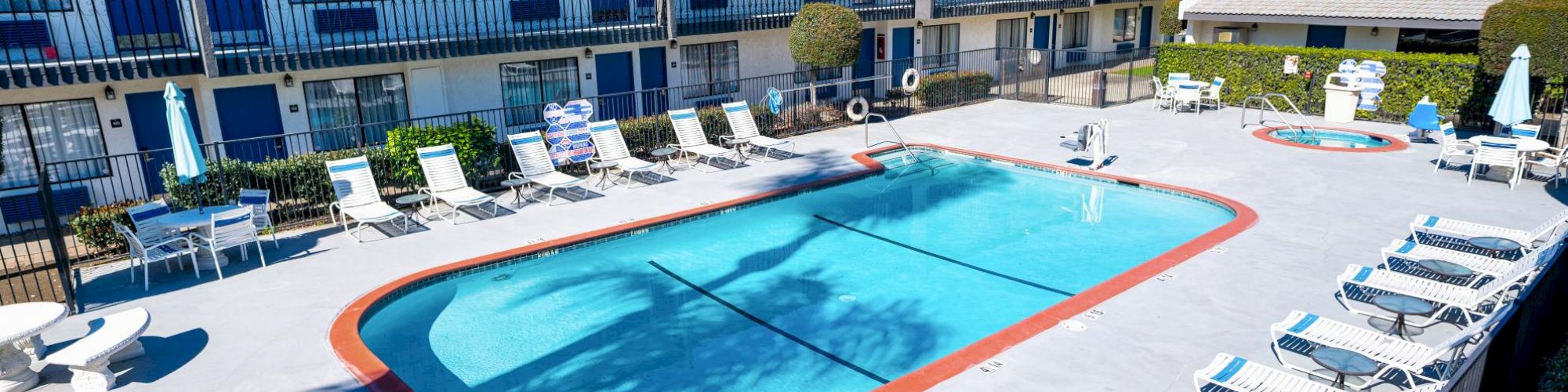 A hotel courtyard with a swimming pool, lounge chairs, and two-story buildings in the background, surrounded by a clean, paved area.