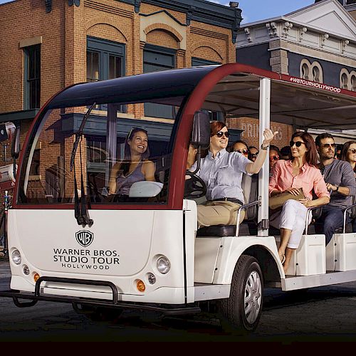 A group of people are taking a Warner Bros. Studio Tour in an open-air tram, driving through a set designed to look like a city street.
