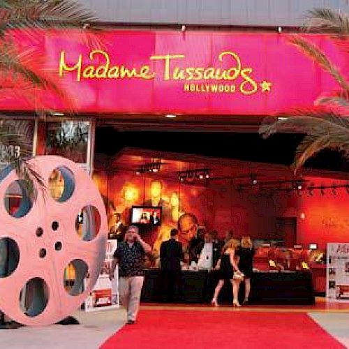 The image shows the entrance of Madame Tussauds Hollywood with film reel decorations and a red carpet leading inside the attraction.