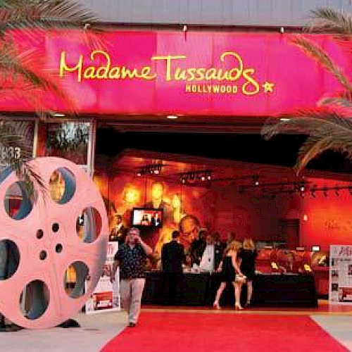 The image shows the entrance of Madame Tussauds Hollywood with film reel decorations and a red carpet leading inside the attraction.