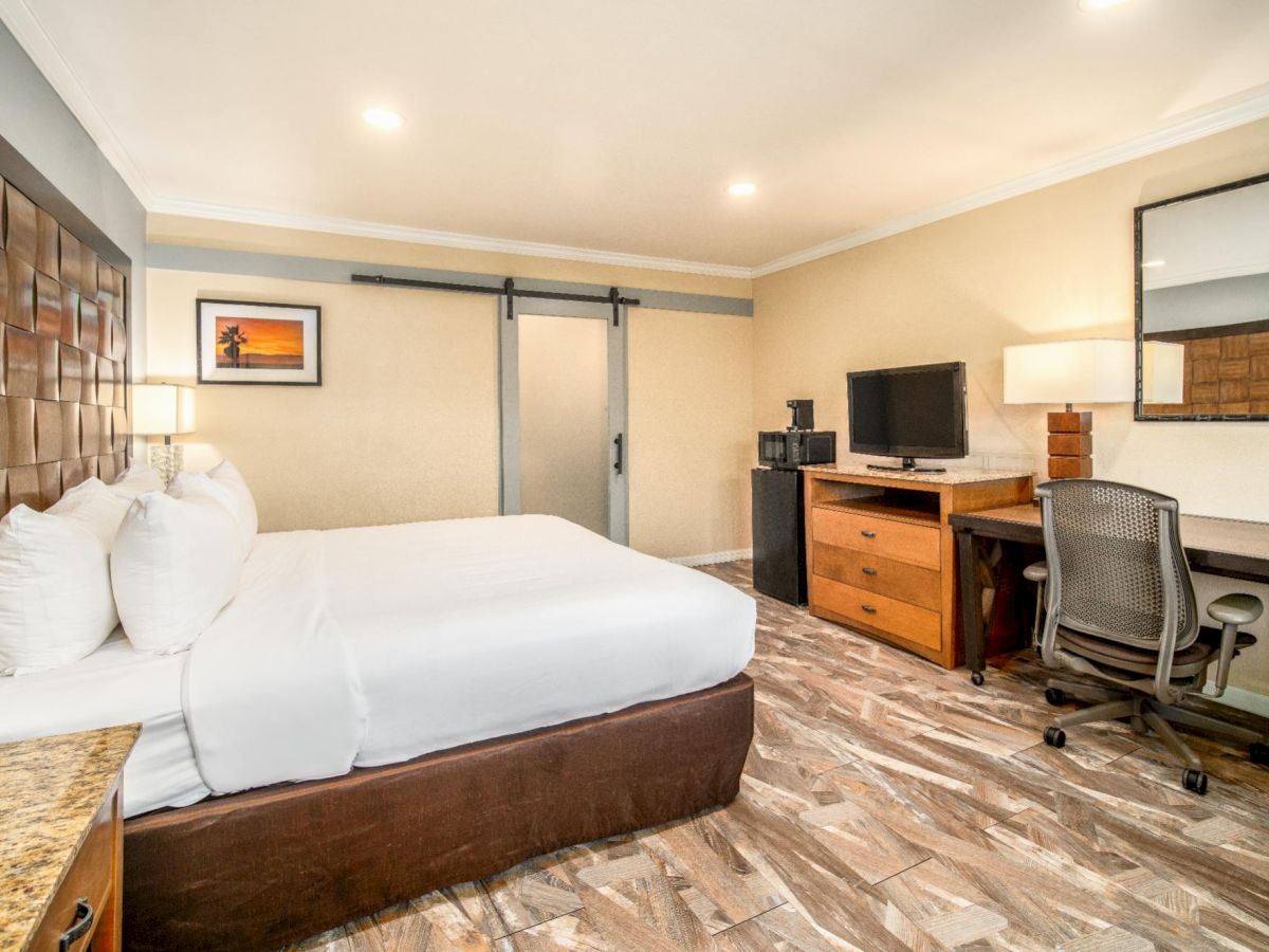 A modern hotel room with a large bed, a wall-mounted TV, a desk with a chair, and a sliding barn door separating the bathroom area ends the sentence.