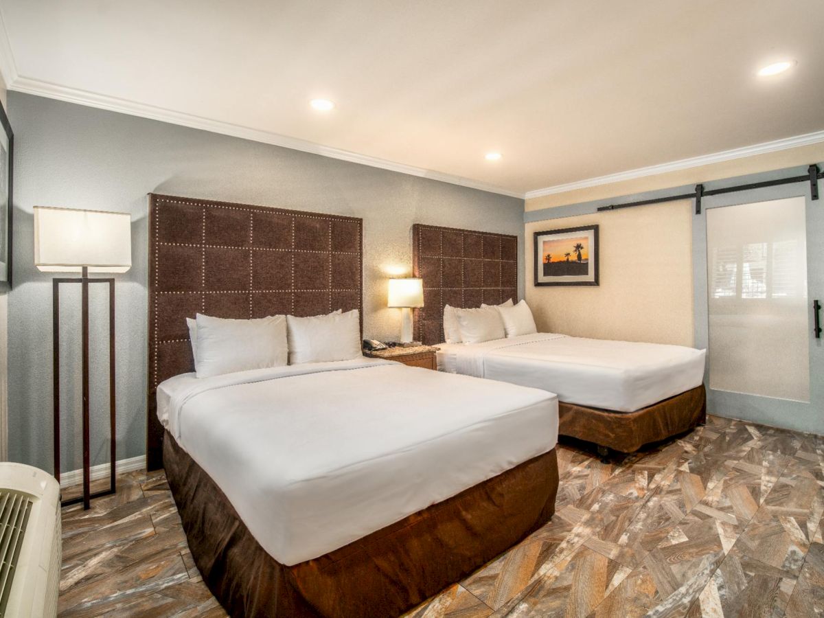 This image shows a hotel room with two double beds, a modern sliding door, a painting, a lamp, and an air conditioning unit near the window.