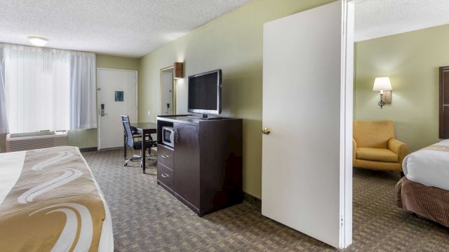 A hotel room with two beds, a desk, a TV, and an armchair.