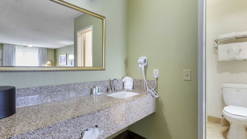 A bathroom with a granite countertop, large mirror, single sink, and toilet.