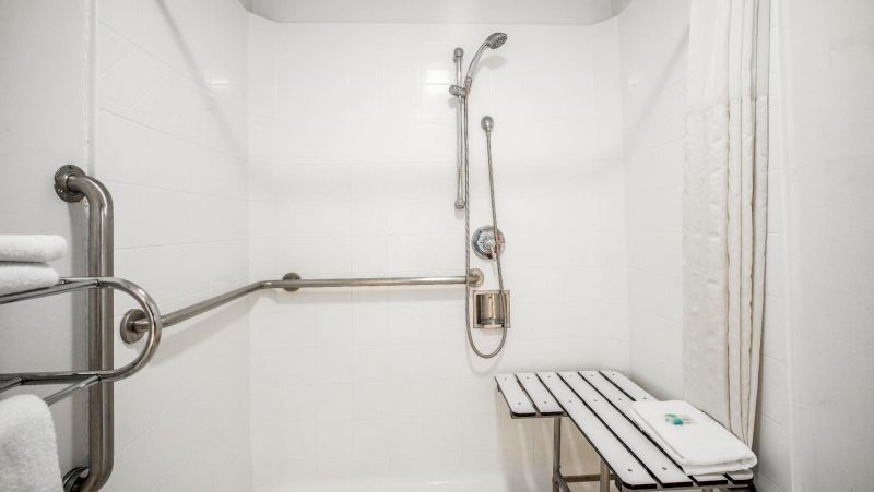 A clean and modern bathroom shower with grab bars, a shower bench, and a rainfall showerhead.