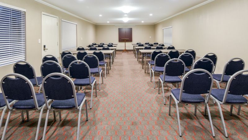A meeting room with rows of chairs and tables, beige walls, and recessed lighting.