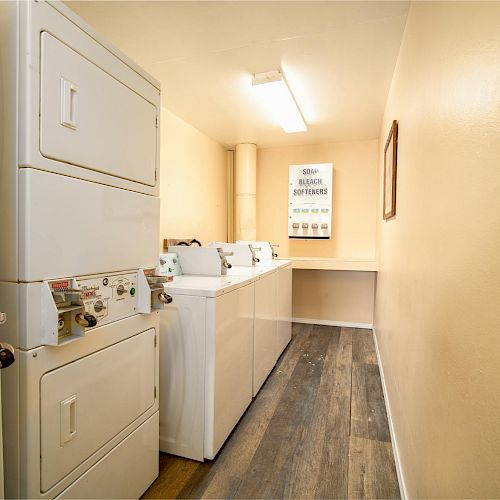 The image shows a small laundry room with off-white walls, coin-operated washing machines and dryers, and a fluorescent ceiling light.