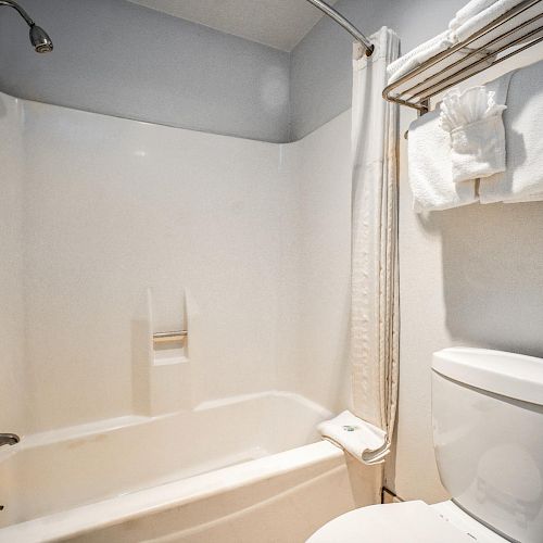 A bathroom with a bathtub-shower combo, a white toilet, towel rack with folded towels, and a grab bar beside the tub.