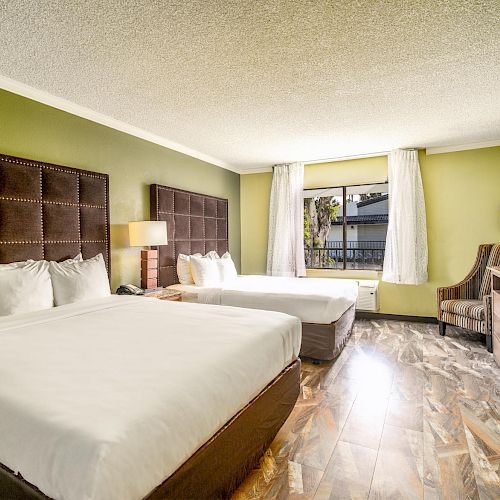 The image shows a hotel room with two large beds, a nightstand, a lamp, a TV on a dresser, a chair, and a window with curtains.