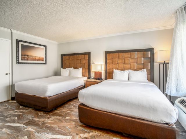 A hotel room with two beds, a picture frame on the wall, and a window with curtains.