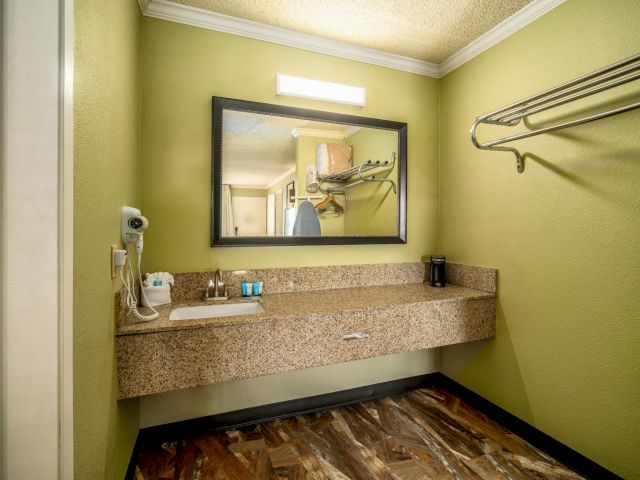 A bathroom with a granite countertop, mirror, sink, hair dryer, and towel rack.