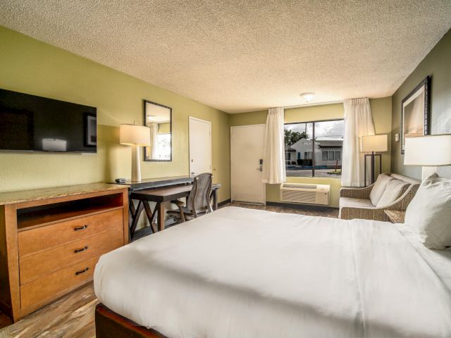 A wide view of a hotel room with a large bed, desk, chair, sofa, and window.