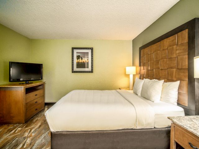 A hotel room with a large bed, TV, and dresser