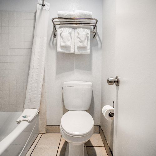 A bathroom with a toilet, bathtub, shower curtain, and towel rack holding towels. There's also a toilet paper holder on the wall.