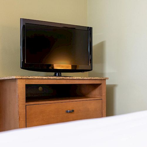 The image shows a flat-screen TV on a wooden dresser with a granite top in a room with light-colored walls.