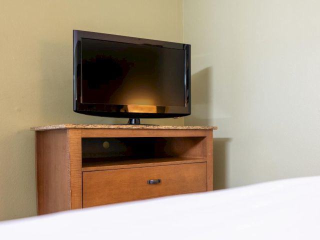 A flat-screen TV on top of a wooden cabinet with a marble countertop and a single drawer.
