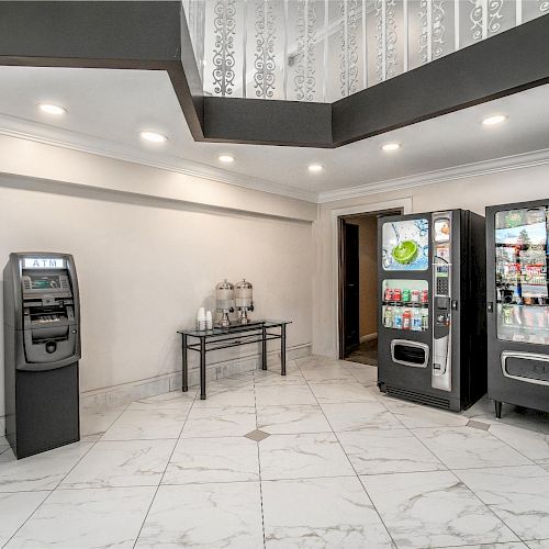 The image features an ATM, two vending machines, and a table with water dispensers in a white tiled room with recessed lighting.