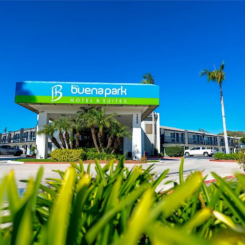 An exterior view of Buena Park Hotel & Suites with clear signage, surrounded by palm trees and bright landscaping on a sunny day, blue sky above.