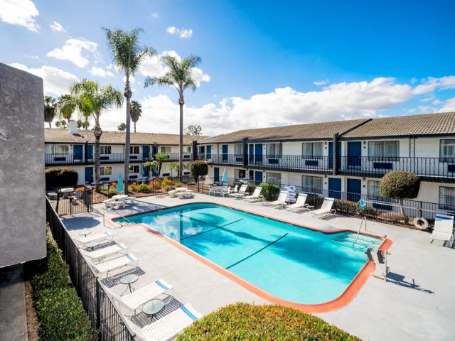 A hotel pool area with lounge chairs, palm trees, and a building in the background.