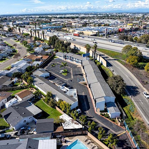 An aerial view of residential houses near a main road, with commercial buildings and a highway visible in the background under a partly cloudy sky.