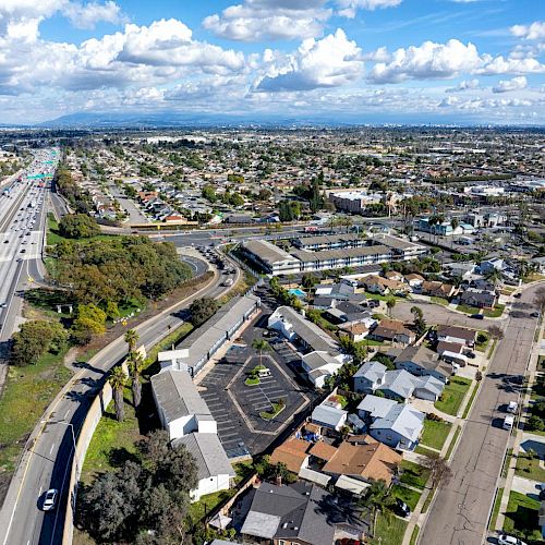 The image shows an aerial view of a suburban area with houses, a highway on the left side, and commercial buildings. The sky is partly cloudy.