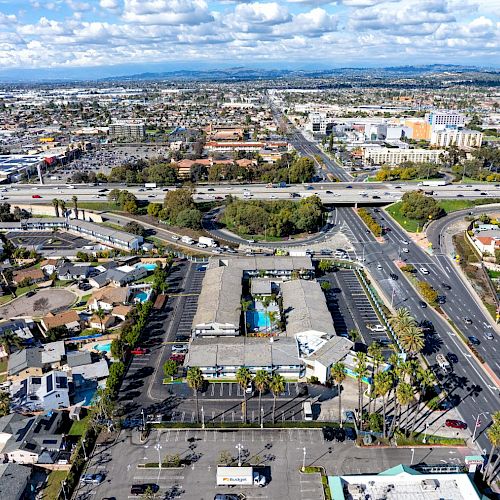 An aerial view of a sprawling suburban area with roads, houses, commercial buildings, and intersecting highways under a partly cloudy sky.