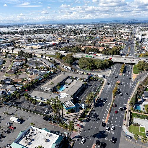 This aerial image shows a busy urban area with multiple roads, buildings, and a freeway overpass, surrounded by residential and commercial areas.