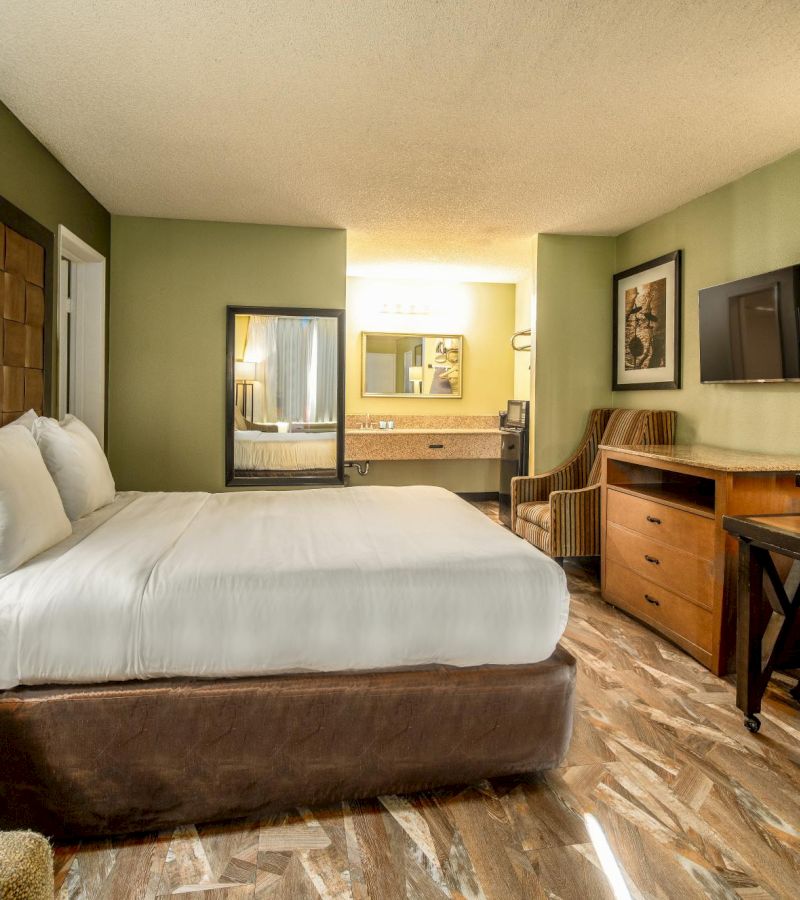 A hotel room with a large bed, desk, chair, and TV