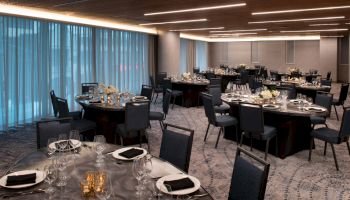 An elegant dining room setup with round tables, each adorned with black napkins, cutlery, glassware, and floral centerpieces.
