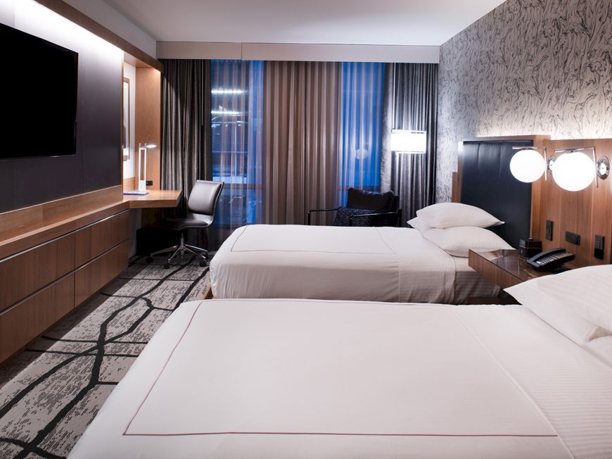 The image shows a modern hotel room with two neatly made beds, a flat-screen TV, a desk with a chair, and stylish decor ending the sentence.