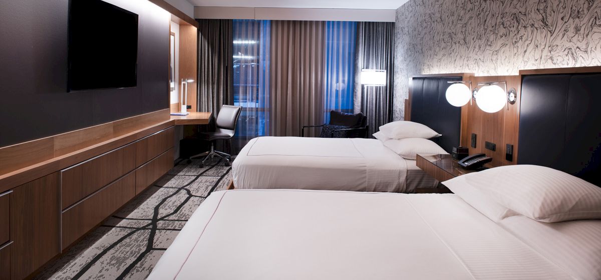 The image shows a modern hotel room with two neatly made beds, a flat-screen TV, a desk with a chair, and stylish decor ending the sentence.