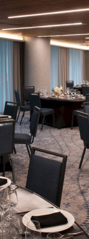 A banquet hall with round tables set for a formal event, featuring dark chairs, elegant table settings, and ambient lighting.